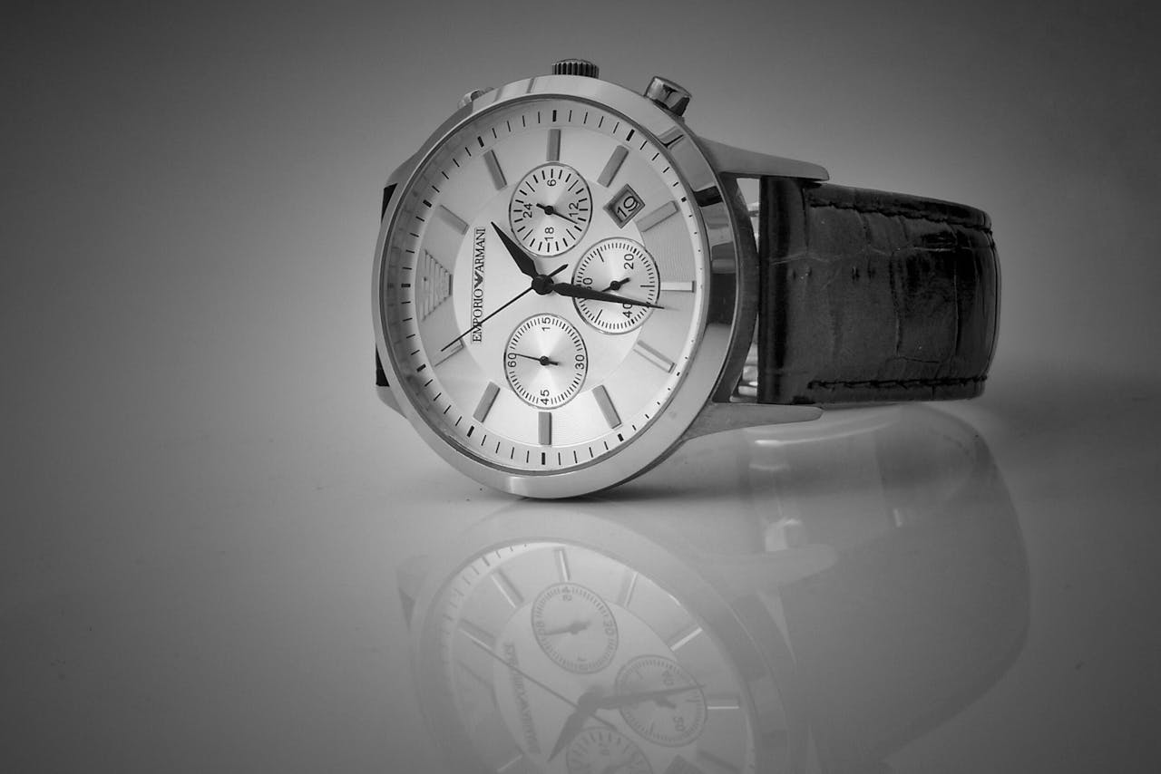Elegant black and white close-up of a luxury wristwatch with a reflective stainless steel body and leather strap.